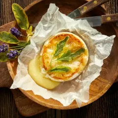 Camembert au barbecue, fondant et doré, servi sur papier sulfurisé avec des herbes aromatiques et des fleurs de lavande. Un délice à partager.