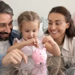 Rodzina z dzieckiem wrzuca monety do świnki-skarbonki.