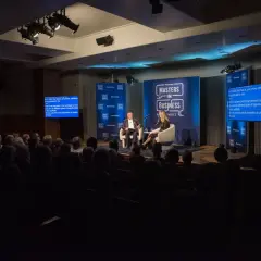 Conference photography captures a panel discussion on a stage with two speakers, audience members in the foreground, and Bloomberg branding.