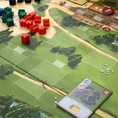 Drewniane pionki w grze planszowej Caylus 1303 na zielonej planszy z polami i drzewami.