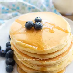 Pancake con albumi soffici e dorati, guarniti con mirtilli freschi e sciroppo d'acero.
