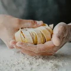 Dłonie trzymające świeży, pokrojony makaron tagliatelle, oprószony mąką.