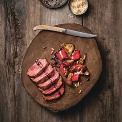 Saftige Tagliata di Manzo mit gebratenen Pilzen und Paprika auf einem rustikalen Holzbrett, garniert mit Pinienkernen und Balsamico.