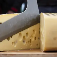 Un coltello affilato taglia un formaggio con i buchi, rivelando la sua consistenza invitante.