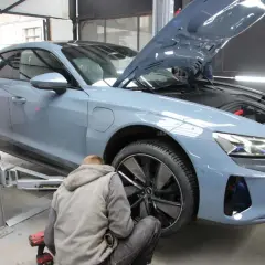 Mechanik przykręca koło w szarym samochodzie elektrycznym na podnośniku. Szybka odpowiedź na pytanie: ile trwa zmiana opon?