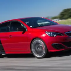 Czerwony Peugeot 308 GTI z czarnym tyłem na torze wyścigowym, dynamicznie pokonujący zakręt.