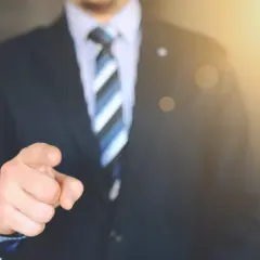Mężczyzna w garniturze wskazuje palcem, sugerując, jak sprawdzić, kto jest właścicielem mieszkania.