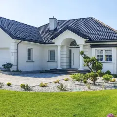 Nowoczesny dom z białą elewacją, ciemnym dachem i zadbanym ogrodem.