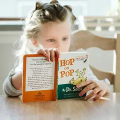Dziewczynka czyta książki do czytania po angielsku, w tym "Hop on Pop" Dr. Seussa.