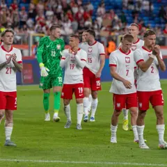Piłkarze reprezentacji Polski w białych strojach z orzełkiem na piersi, klaskający na murawie. Ich pozycja w tabeli mistrzów Polski w piłce nożnej jest nieznana.