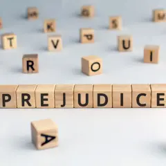 Des cubes en bois forment le mot "PREJUDICE", symbolisant le préjudice moral psychologique. D'autres lettres flottent autour.