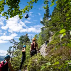 Äventyr vid Ramundberget: klättrare på klippvägg, linbana i skyn, vacker utsikt.