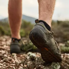 Niski profil butów trekkingowych, z widoczną wysokością cholewki, podczas marszu po kamienistym, suchym terenie.