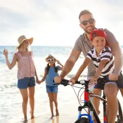 Famiglia felice in bicicletta sulla spiaggia, un'idea per le tue prossime idee viaggio con bambini in Italia.