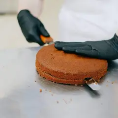 Manos enguantadas cortan un bizcocho redondo, preparándolo para ser la base de una deliciosa masa de tarta.
