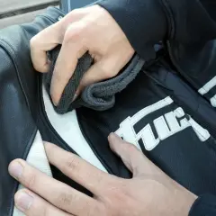 Manos limpian chaqueta de moto de cuero negro con detalles blancos. Aprende como lavar una chaqueta de moto.