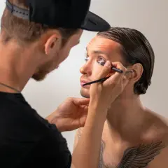 Un truccatore applica l'eyeliner a un modello, creando un look audace.