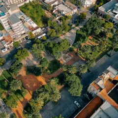 Un parco urbano rigenerato, con palme e alberi, circondato da edifici residenziali e commerciali.