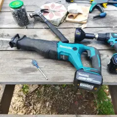 Outils Makita, marque d'outillage américain, prêts pour le travail du bois. Une scie alternative, une perceuse, un marteau et des clous sur une table en bois.
