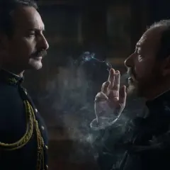 Dwaj mężczyźni w historycznych strojach, jeden w mundurze, drugi z papierosem, w kłębach dymu. Scena z filmu Polańskiego.