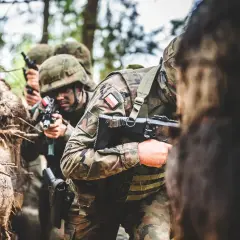 Żołnierze w kamuflażu, z karabinami w rękach, przygotowują się do akcji. To obraz z ćwiczeń, gdzie obowiązkowa służba wojskowa jest ważnym elementem szkolenia.