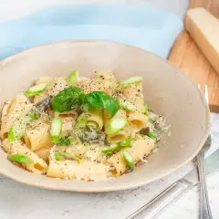 En krämig tallrik med pasta med sparris, toppad med färsk basilika och riven parmesan. En bit parmesan ligger bredvid.