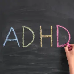 Napis "ADHD" kredą na tablicy, pisany przez rękę.