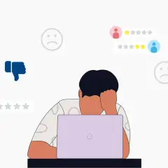 Persona frustrata davanti al laptop, circondata da recensioni negative e pollici in giù. Impara come rispondere alle recensioni negative per migliorare la tua reputazione online.