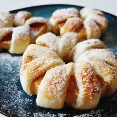 Pyszne ciasto francuskie z jabłkami, posypane cukrem pudrem, prezentuje się apetycznie na granatowym talerzu.
