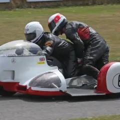Dos pilotos en un sidecar de carreras, uno conduciendo y el otro en la silla lateral. El número 6 en el sidecar. William Dunlop, un nombre asociado con la velocidad.