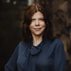Charlotte Al-Khalili, en kvinna med brunt hår och blå ögon, bär en mörkblå blus med rosett.