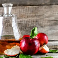 Szklana karafka z bursztynowym płynem, jabłka i liście na drewnianym tle. Idealne składniki, by dowiedzieć się, jak zrobić cydr.
