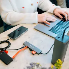 Kobieta pracuje na laptopie, podłączając telefon, dysk zewnętrzny i kartę SD do stacji dokującej USB 3.2.