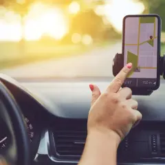 Dłoń z czerwonym lakierem na paznokciach dotyka ekranu telefonu z mapą, korzystając z nawigacji na telefon podczas jazdy.
