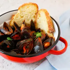 Un invitante guazzetto di cozze in una pentola rossa, accompagnato da pane croccante e una forchetta.