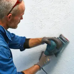 Man slipar en vägg med en excenterslip för att få bort slipdamm innan målning.