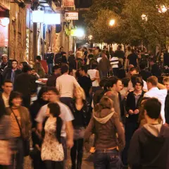 Folla animata in una stretta via di Madrid, tra luci soffuse e insegne luminose, perfetta per la movida.