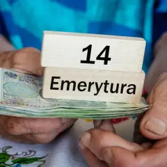 Dłonie trzymają stos banknotów i drewniane klocki z napisem "14 Emerytura".