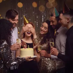 Grupa przyjaciół świętuje urodziny w domu. Jubilatka z zasłoniętymi oczami czeka na niespodziankę z tortem. To świetne, fajne atrakcje na urodziny w domu!