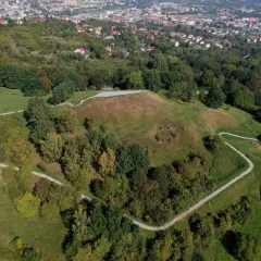 Widok z lotu ptaka na Kopiec Tatarski w Przemyślu, otoczony zielenią i wijącymi się ścieżkami. W oddali widać panoramę miasta.