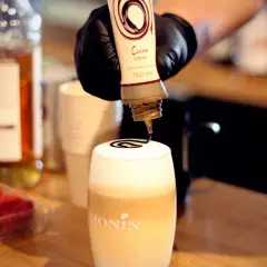 Barista ozdabia gorącą czekoladę do picia syropem kakaowym.