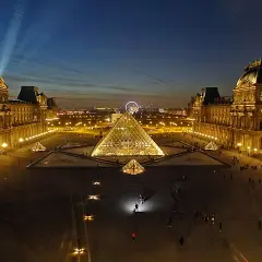 La Pyramide du Louvre illuminée, une belle soirée du 14 juillet. La foule admire le spectacle nocturne.