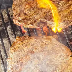 Två saftiga biffar grillas med ved. Flammor slickar köttet som får en perfekt yta.