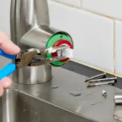 A hand uses pliers to remove a faucet cartridge, a key step in learning how to replace faucet cartridge.