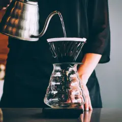 Parzenie kawy metodą drip: gorąca woda powoli przelewa się przez filtr z kawą do szklanego naczynia.