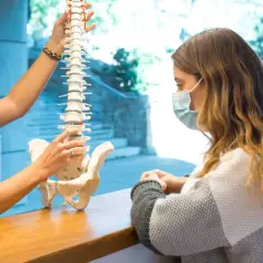 Fizjoterapeuta pokazuje pacjentce model kręgosłupa, wyjaśniając, jak wygląda dyskopatia lędźwiowa i przepuklina kręgosłupa.