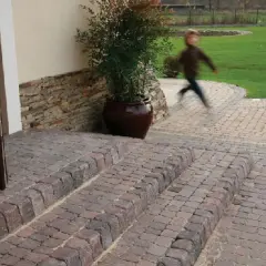 Schody z polbruku prowadzą do drzwi. W tle dziecko biegnie po trawniku.