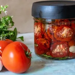 Glas mit eingelegten, sonnengetrockneten Tomaten, frischen Tomaten, Knoblauch und Basilikum. Perfekt für die Konservierung von Tomaten.