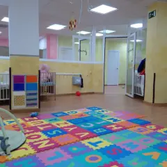 Un espacio acogedor en una escuela infantil o guardería, con cunas, alfombras de letras y juguetes para los más pequeños.