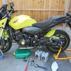 Moto Honda Hornet gialla pronta per cambiare l'olio di lubrificazione del motore. Attrezzi e olio a terra.
